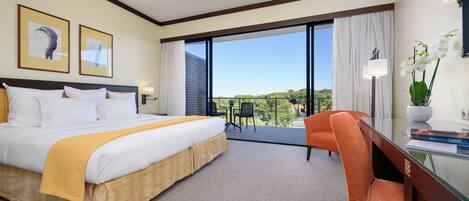 Habitación de hotel con una cama grande, un escritorio, una silla y un balcón con vistas al paisaje.