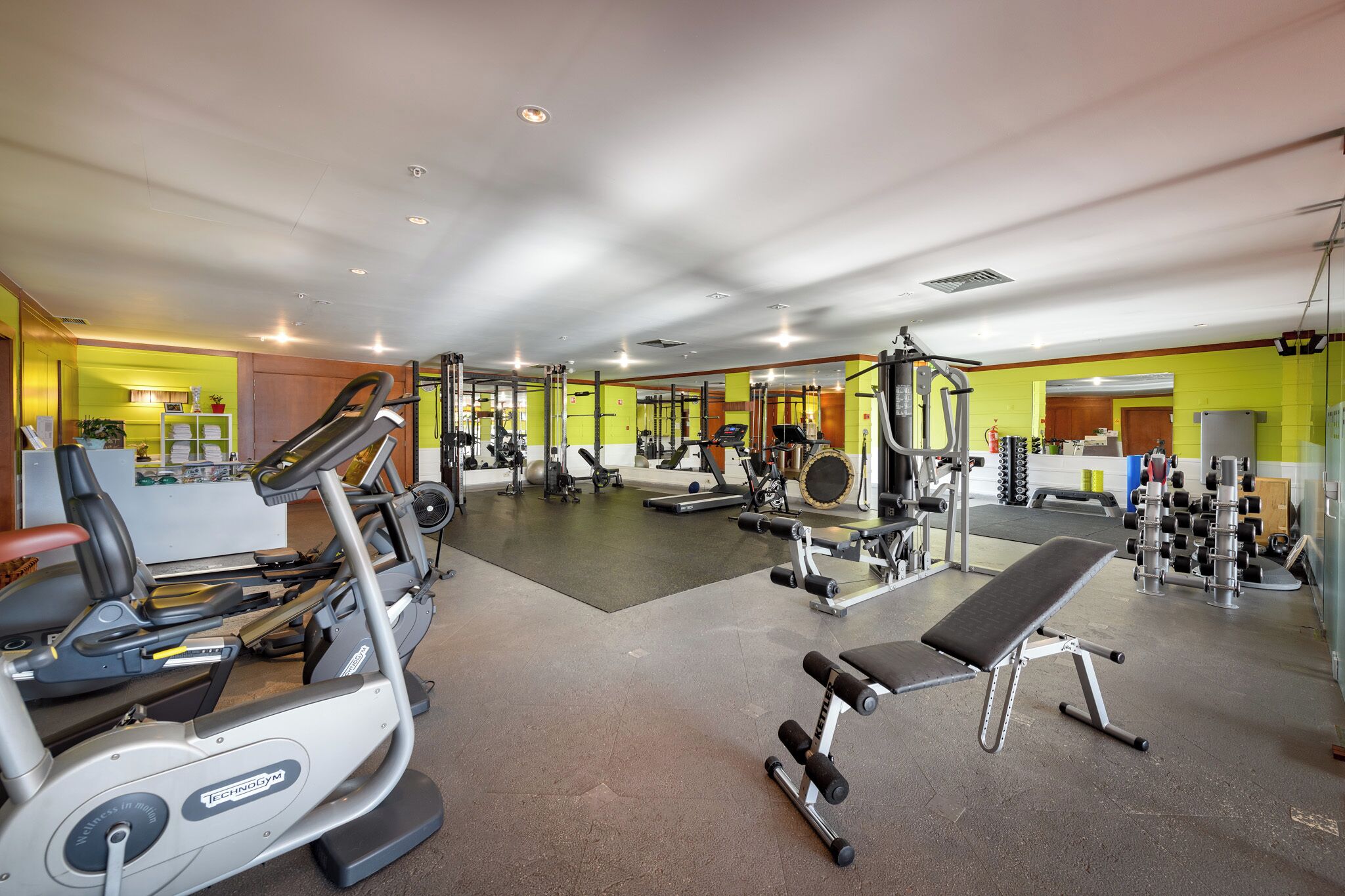 Een fitnessruimte met diverse trainingsapparaten, waaronder loopbanden, een bankje en krachtapparaten.