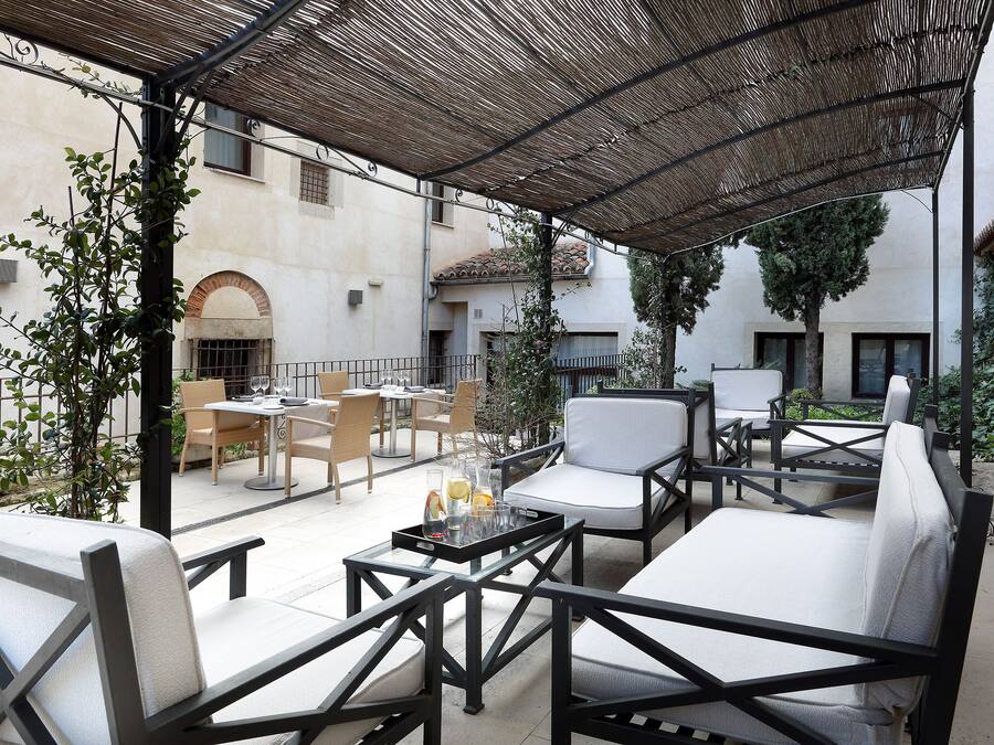Un patio al aire libre con arreglos de asientos, incluyendo sillas y un sofá, bajo una pérgola con sombra.