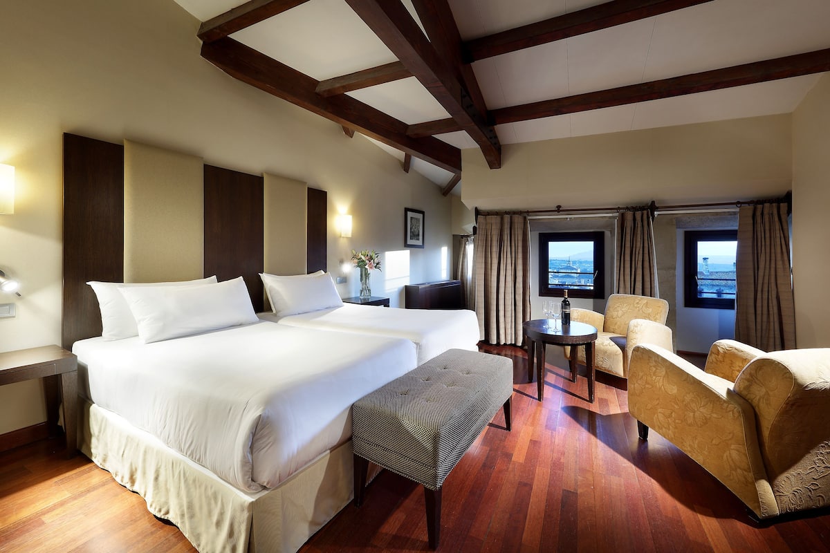 A hotel room with a large bed, two armchairs, a small table, and a TV.
