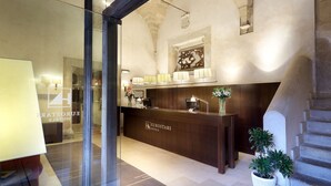 A reception area with a wooden counter, a glass door, and a stone wall. - Eurostars Palacio Santa Marta (Trujillo)