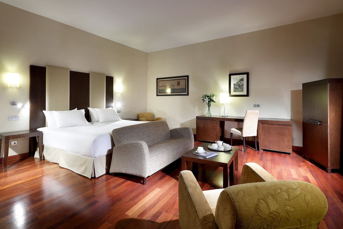 A hotel room with a bed, sofa, desk, chair, and a cabinet.
