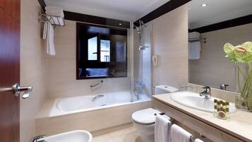 A modern bathroom with a bathtub, a toilet, a bidet, and a large mirror.
