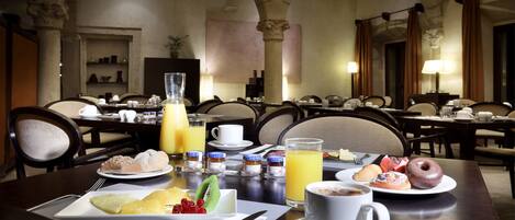 A breakfast setting with a variety of dishes, including pastries, fruits, and beverages, in a dining area with multiple tables and chairs.