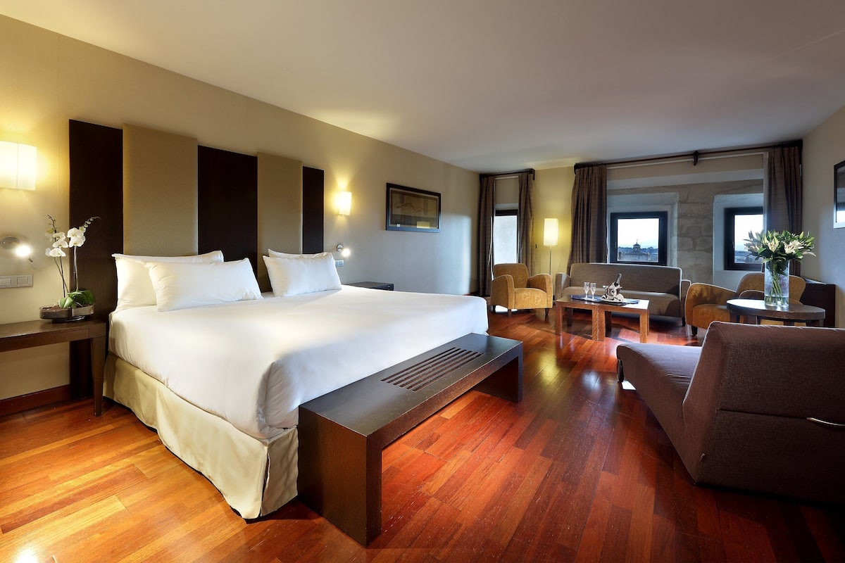A hotel room with a large bed, a desk, a sofa, and a dining area.