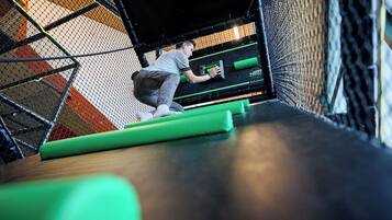A person climbing a netted obstacle course with green mats and a black wall.
