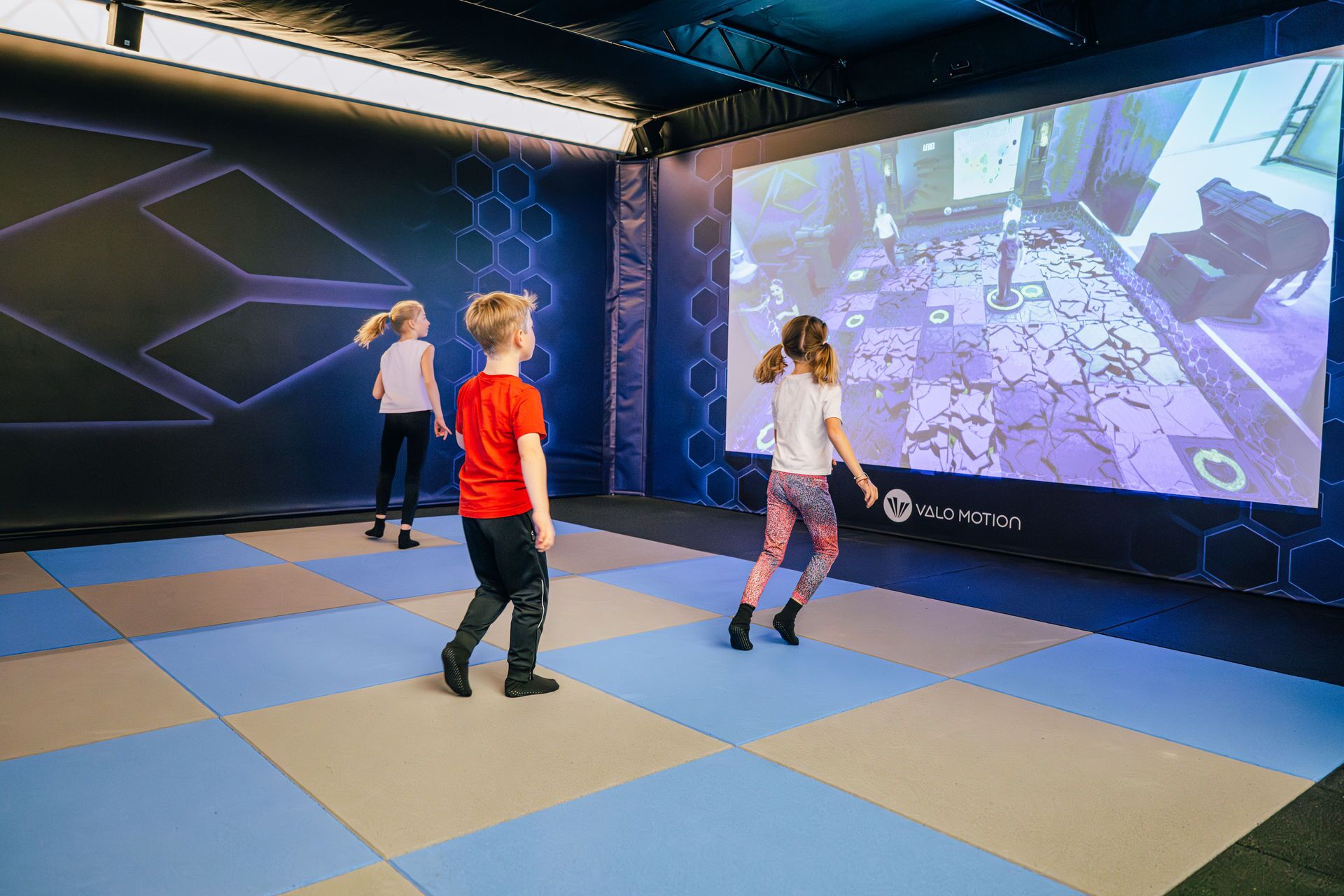 A group of children playing a video game in a room with a large screen displaying a game interface.