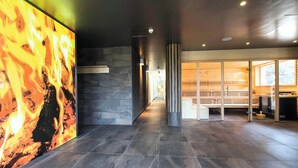 Un moderno vestíbulo de hotel con una pared de piedra, una pantalla digital con motivos de fuego y un separador de vidrio que da a una zona de estar.