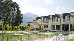 Un hotel moderno con piscina, rodeado por un jardín ajardinado y montañas al fondo.