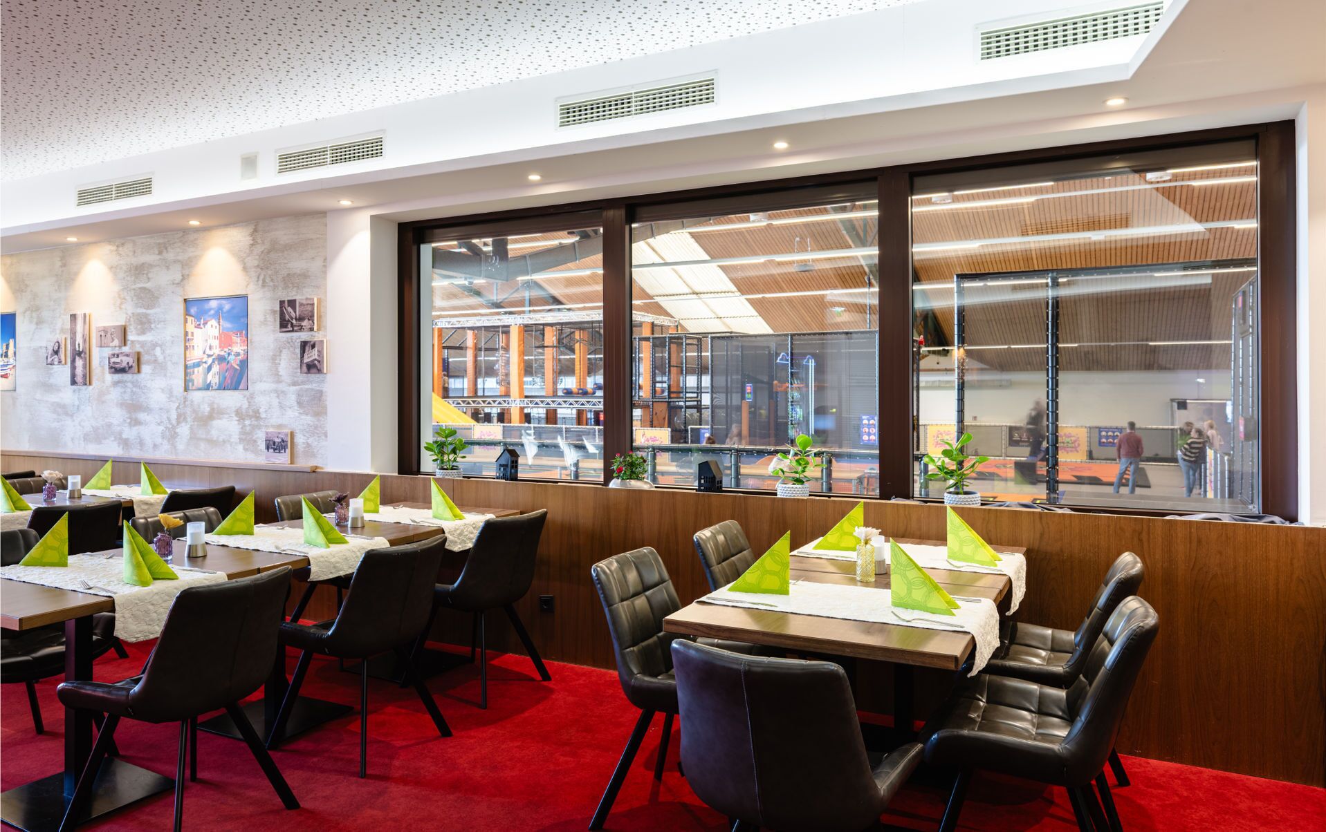 Un restaurante con mesas dispuestas para comer, una alfombra roja y vistas a un área exterior a través de amplias ventanas.
