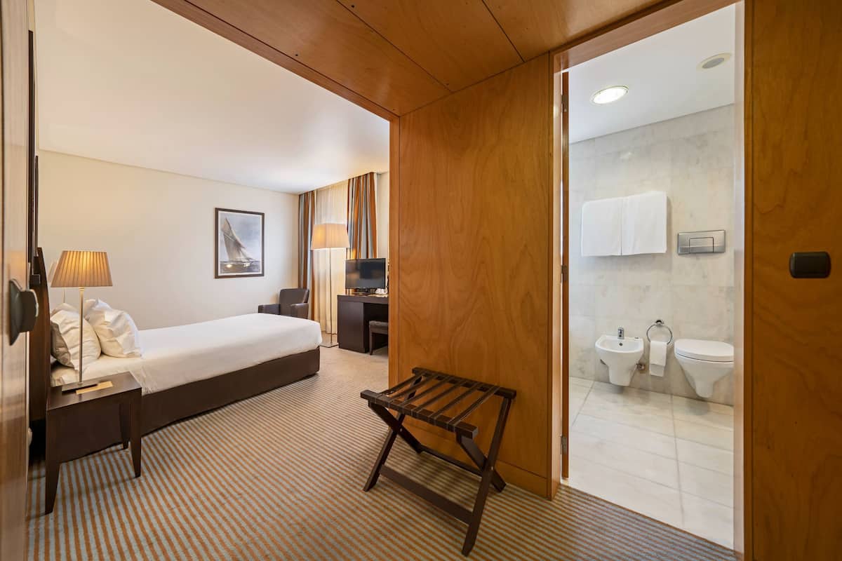 Ein Hotelzimmer mit Bett, Nachttisch, Lampe und einer Holzbank.