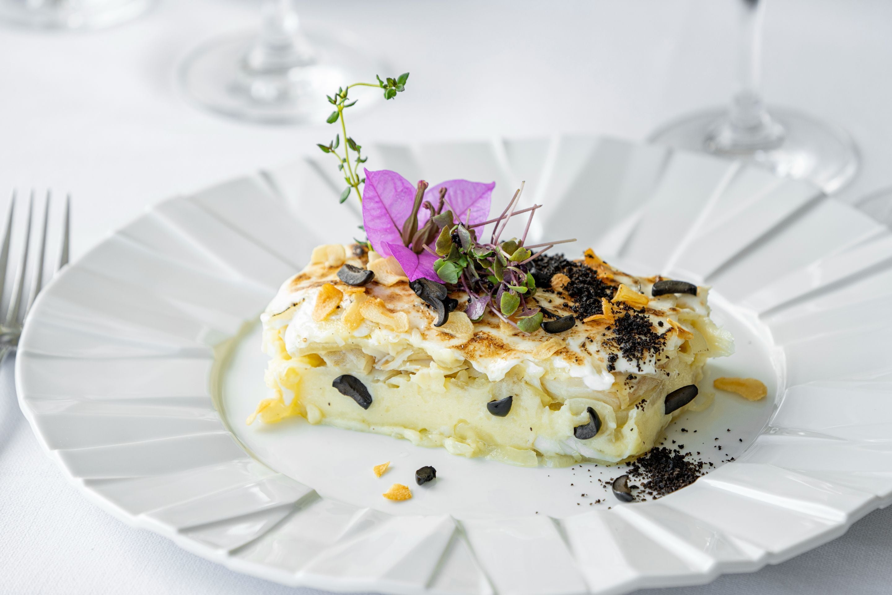 A white plate with a slice of layered food, garnished with a purple flower and black seeds.