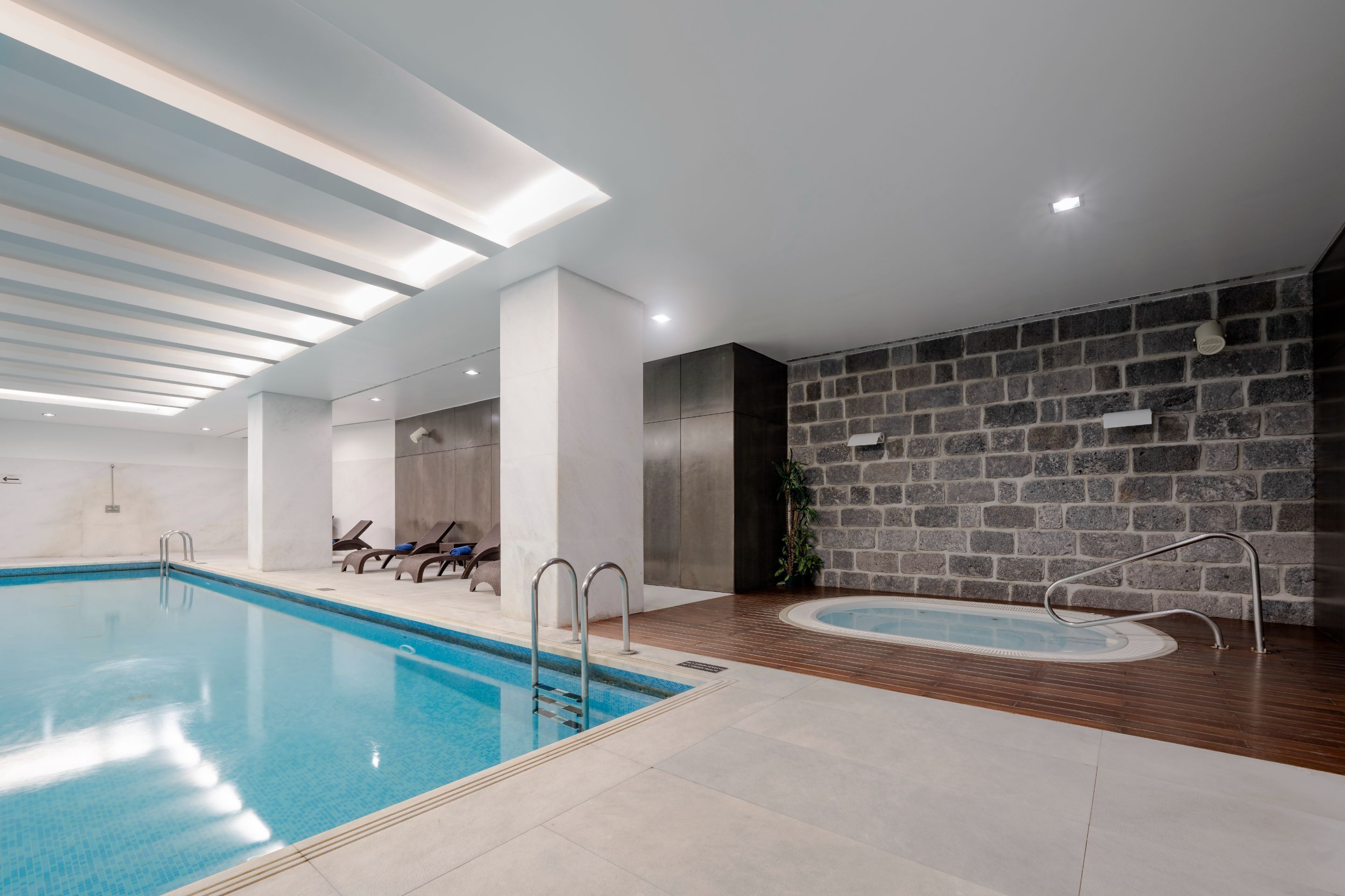 Una piscina interior con agua cristalina, un deck de madera y una pared de piedra.