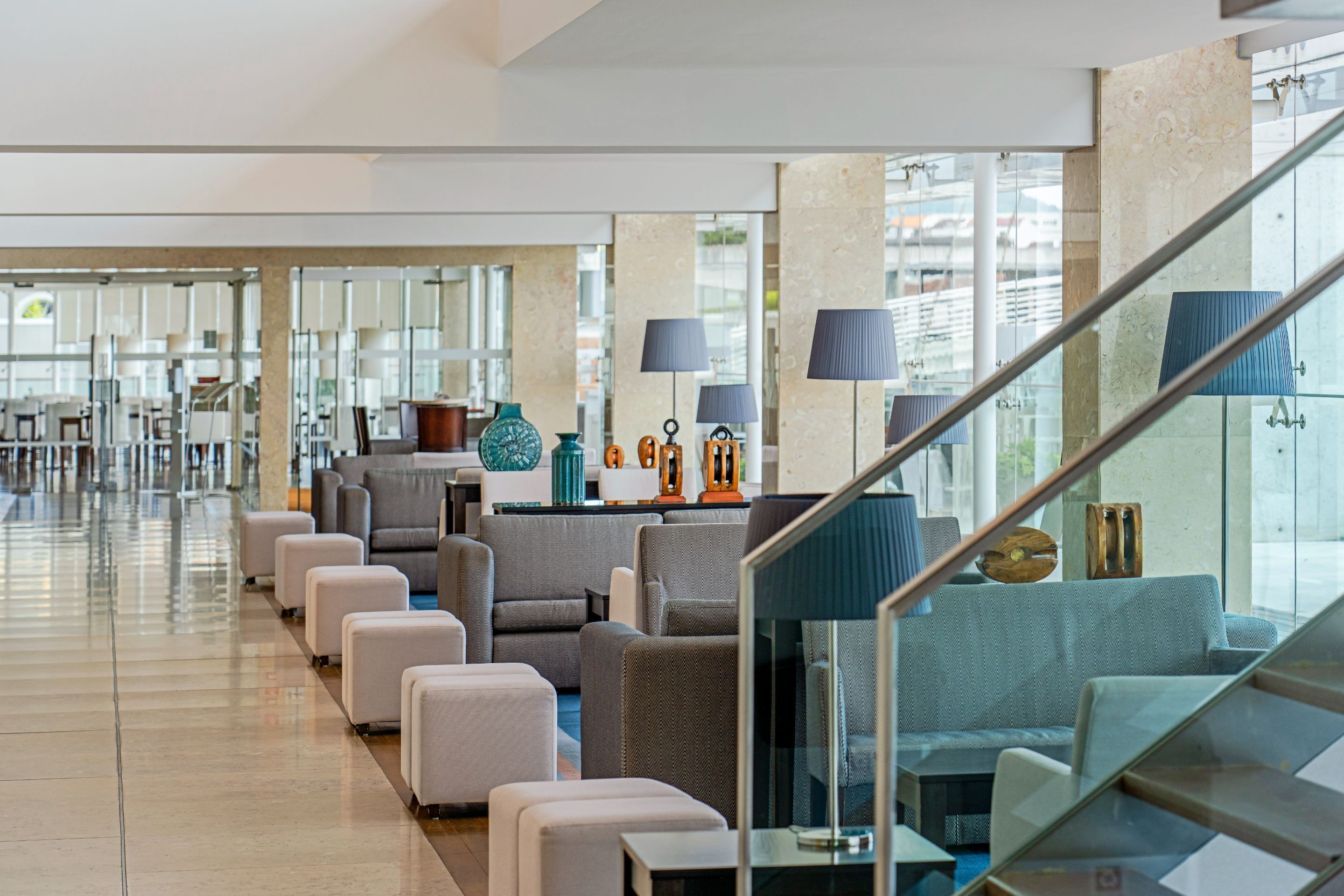 A modern hotel lobby with a spacious seating area, a staircase, and large windows.