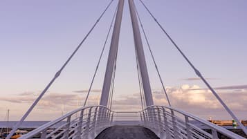 A bridge with a metal deck and white railings, leading to a body of water.