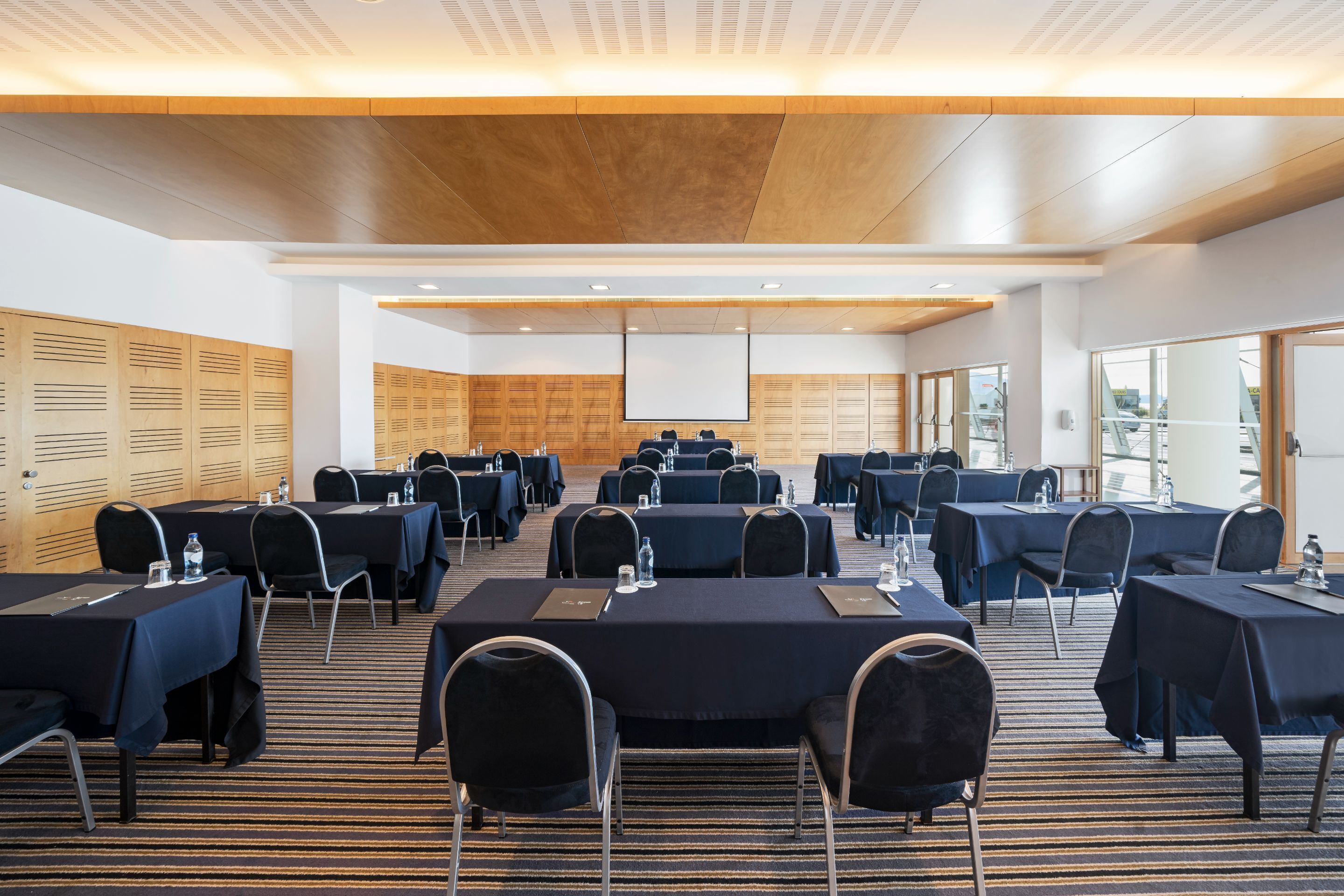 Un salón de conferencias con varias mesas y sillas, equipado con botellas de agua y tarjetas de identificación.