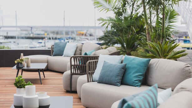 A modern outdoor seating area with a sofa and chairs, a small table with decorative items, and a view of a marina with boats. - Hotel Marina Atlântico (Ponta Delgada)