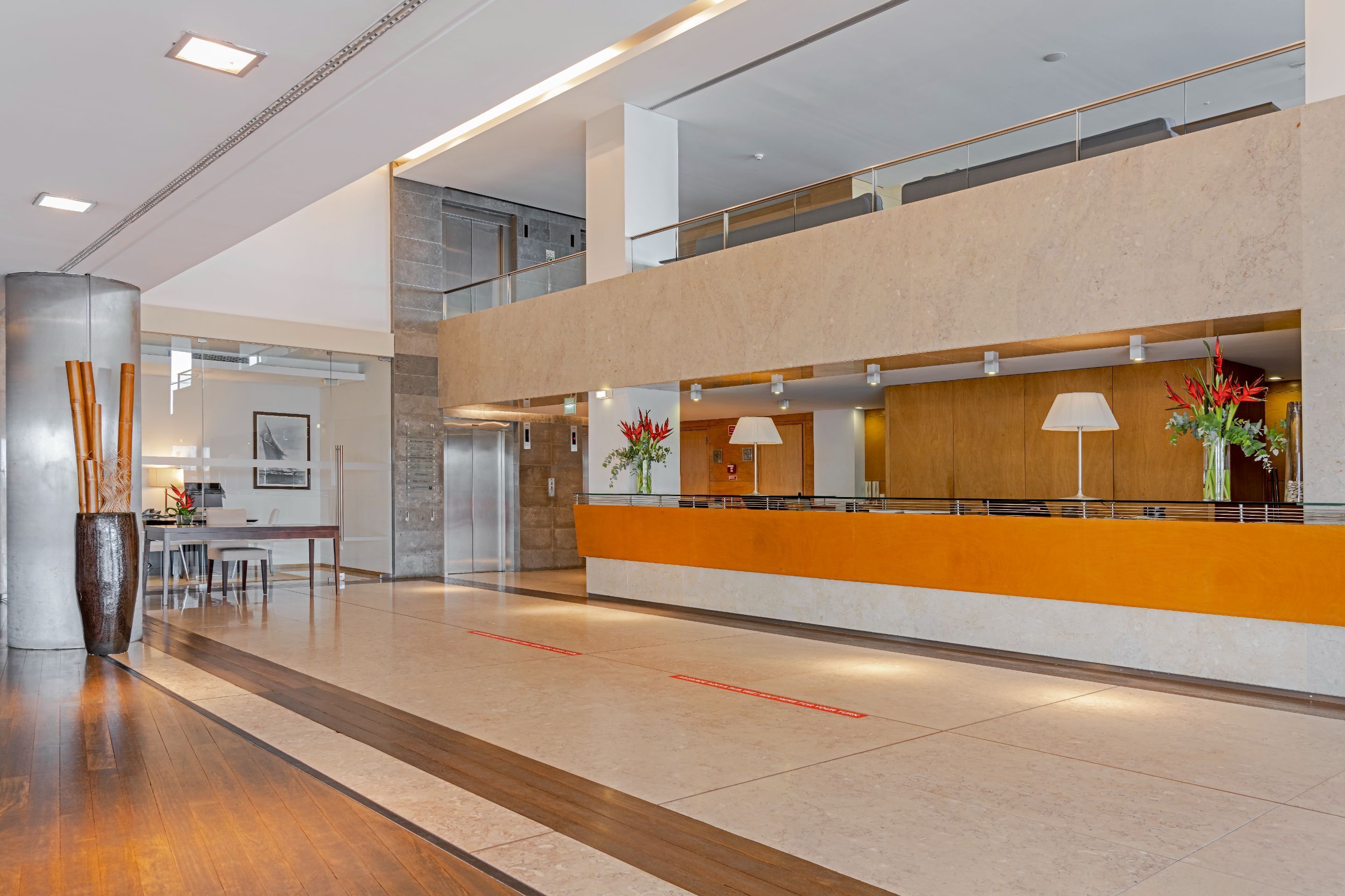 A spacious lobby with a reception desk, a staircase, and a high ceiling with recessed lighting.