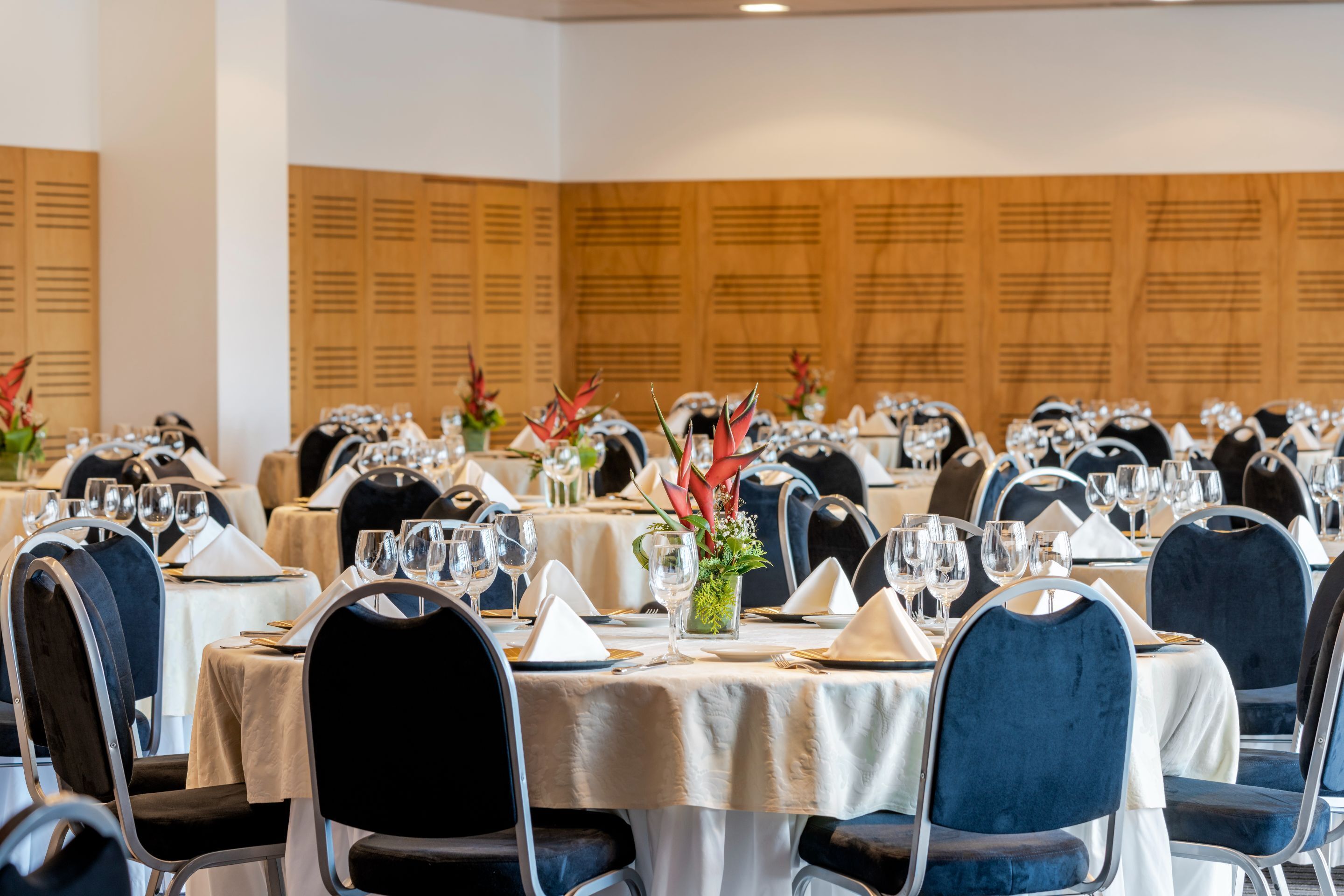 A banquet hall with round tables set for dining, each with a white tablecloth, chairs, and glassware.
