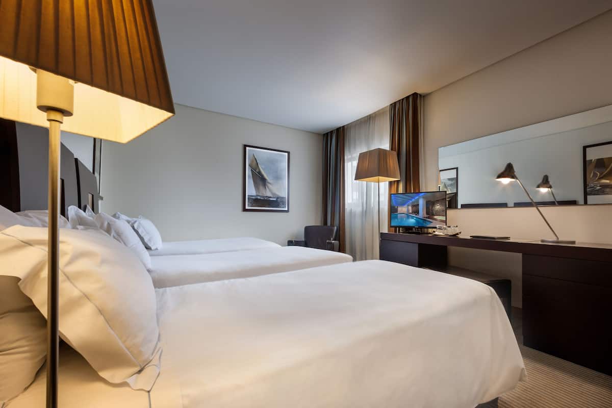 Ein Hotelzimmer mit zwei Betten, einem Schreibtisch mit Computer, einem Fernseher und einem großen Spiegel.