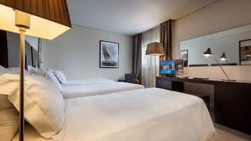 Quarto de hotel com duas camas, uma escrivaninha com computador, televisão e um espelho grande.