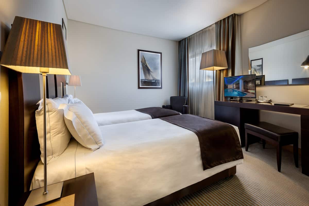 Ein Hotelzimmer mit zwei Betten, einem Schreibtisch, einem Sessel, einem Fernseher und einem großen Spiegel.