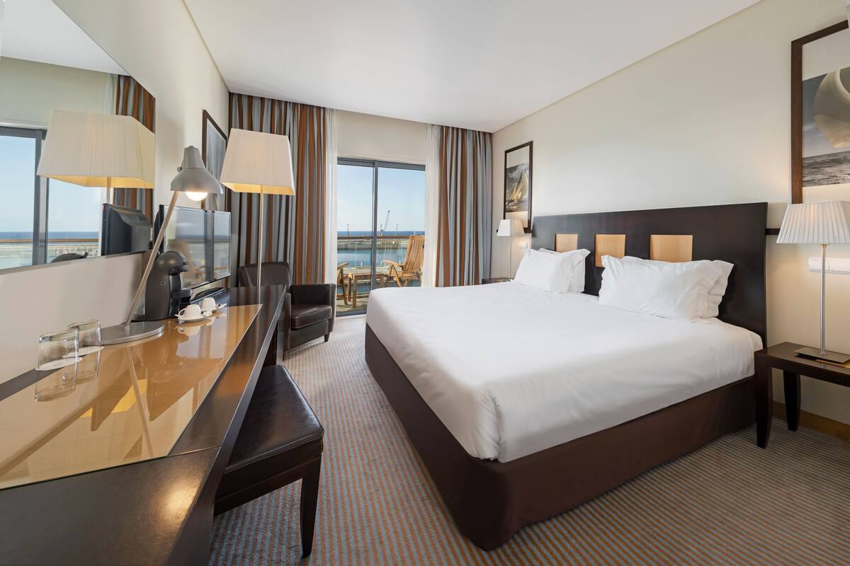 Ein Hotelzimmer mit einem großen Bett, einem Schreibtisch, einem Stuhl, einem Fernseher und Blick aufs Meer.