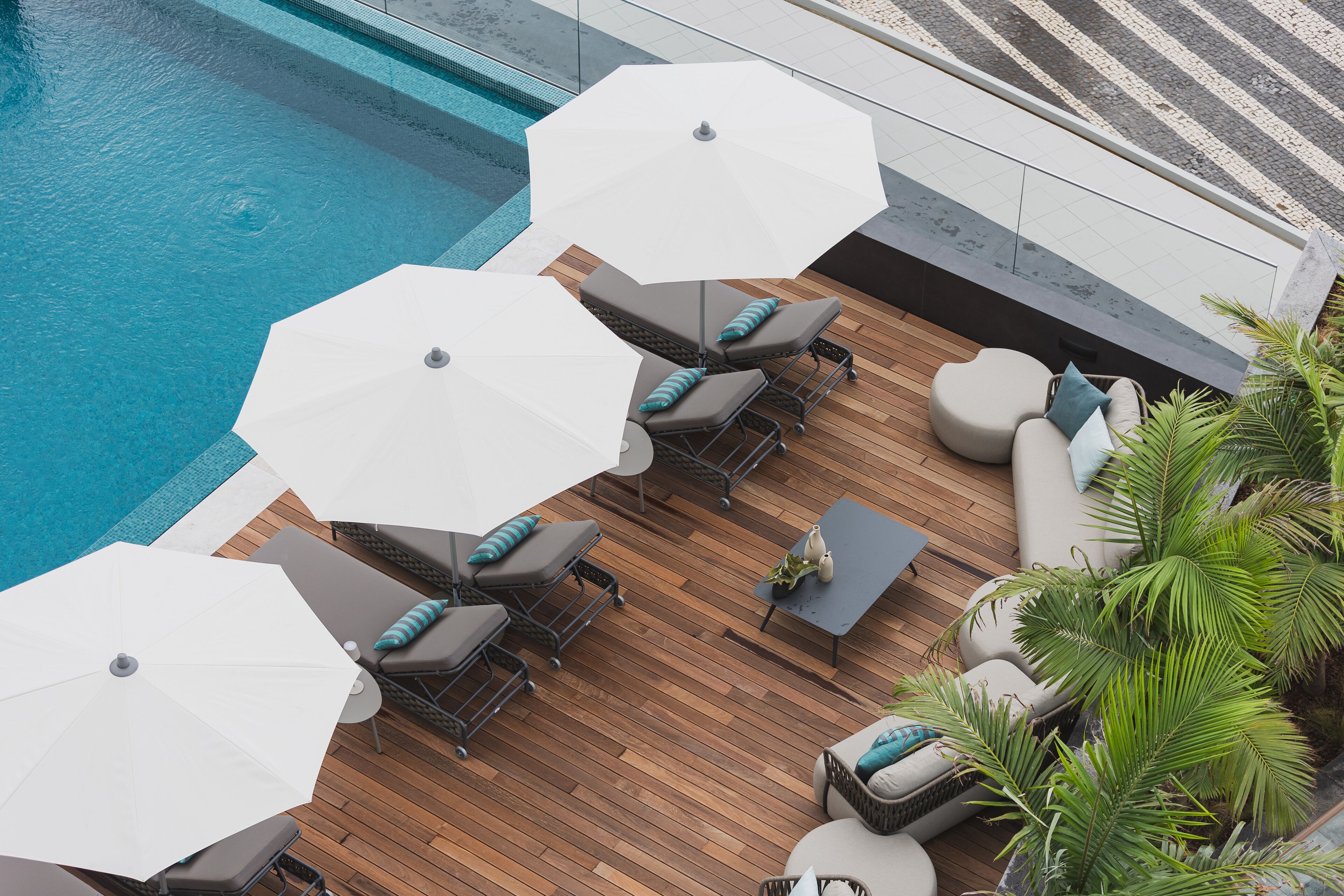 Ein Poolbereich auf dem Dach mit mehreren Liegestühlen und Sonnenschirmen, umgeben von Holzterrasse und Topfpflanzen.