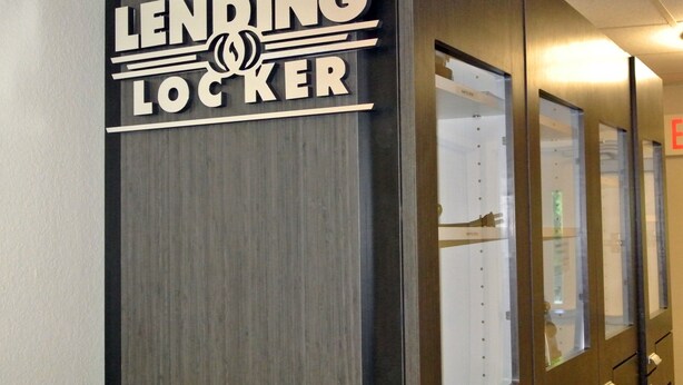 A sign for a lending locker in a hallway with glass doors and a wooden wall. - Candlewood Suites Washington Dulles Sterling by IHG (Sterling)