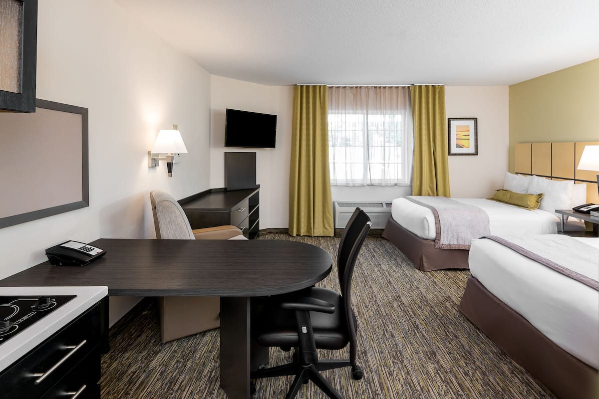 Een hotelkamer met een bed, een bureau met stoel, een aan de muur bevestigde televisie en een raam met gordijnen.