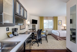 Habitación de hotel con kitchenette, cama, escritorio y televisión.