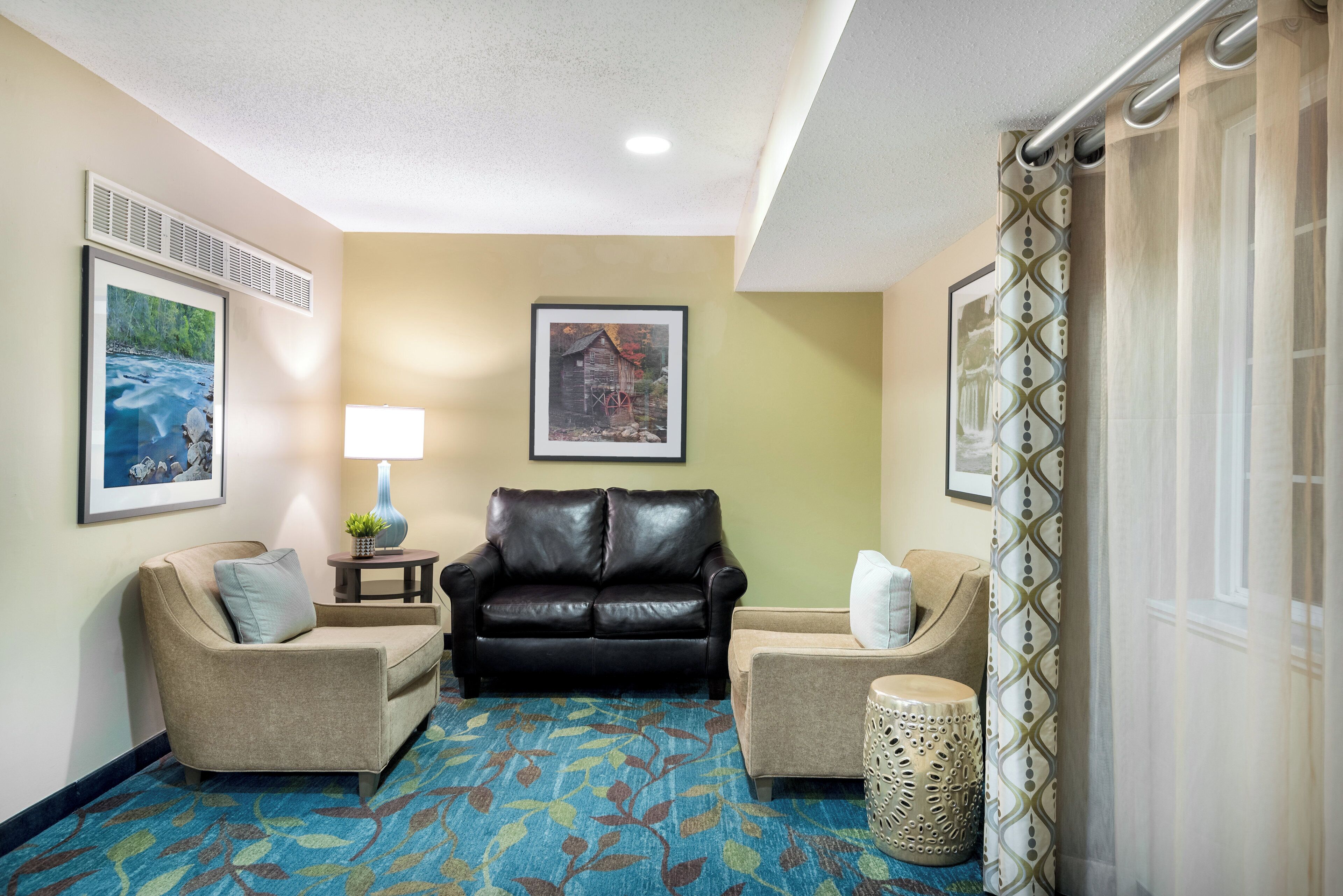 A hotel lobby with a black leather sofa, two armchairs, a patterned carpet, and framed pictures on the walls.