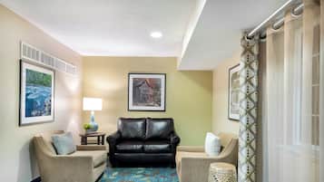 A hotel lobby with a black leather sofa, two armchairs, a patterned carpet, and framed pictures on the walls.
