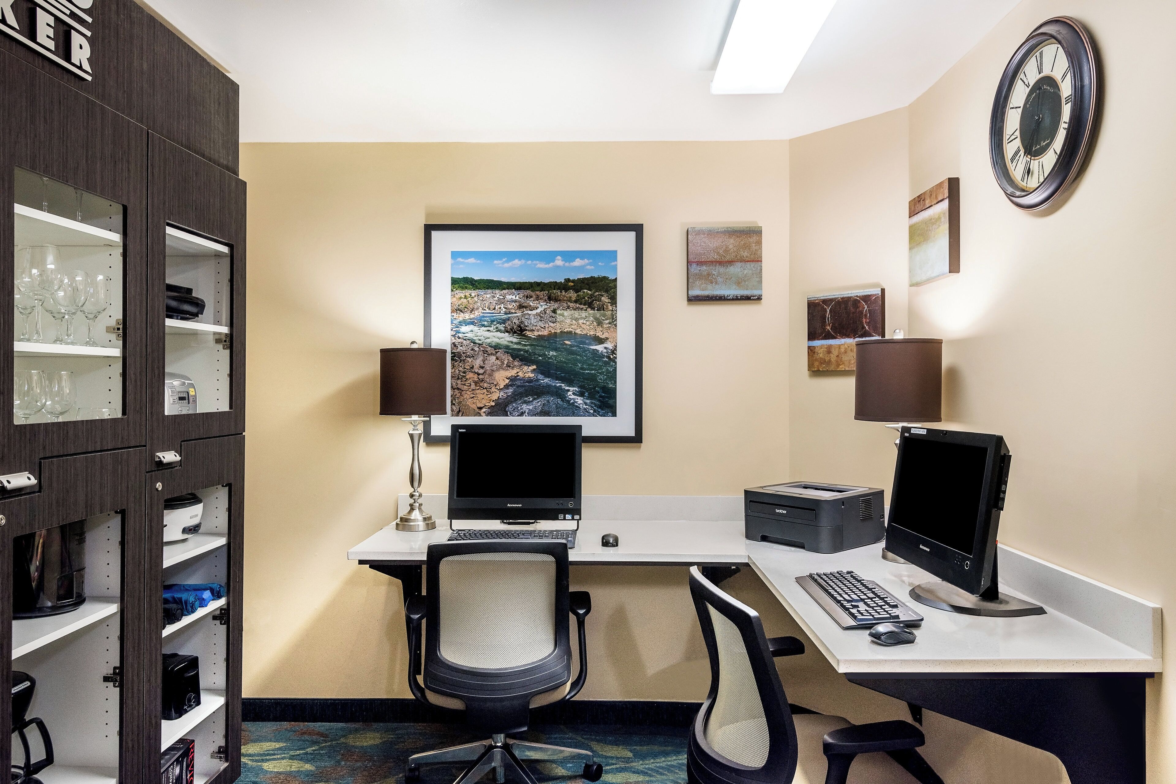 A hotel office with two desks, computers, chairs, and a wall clock.
