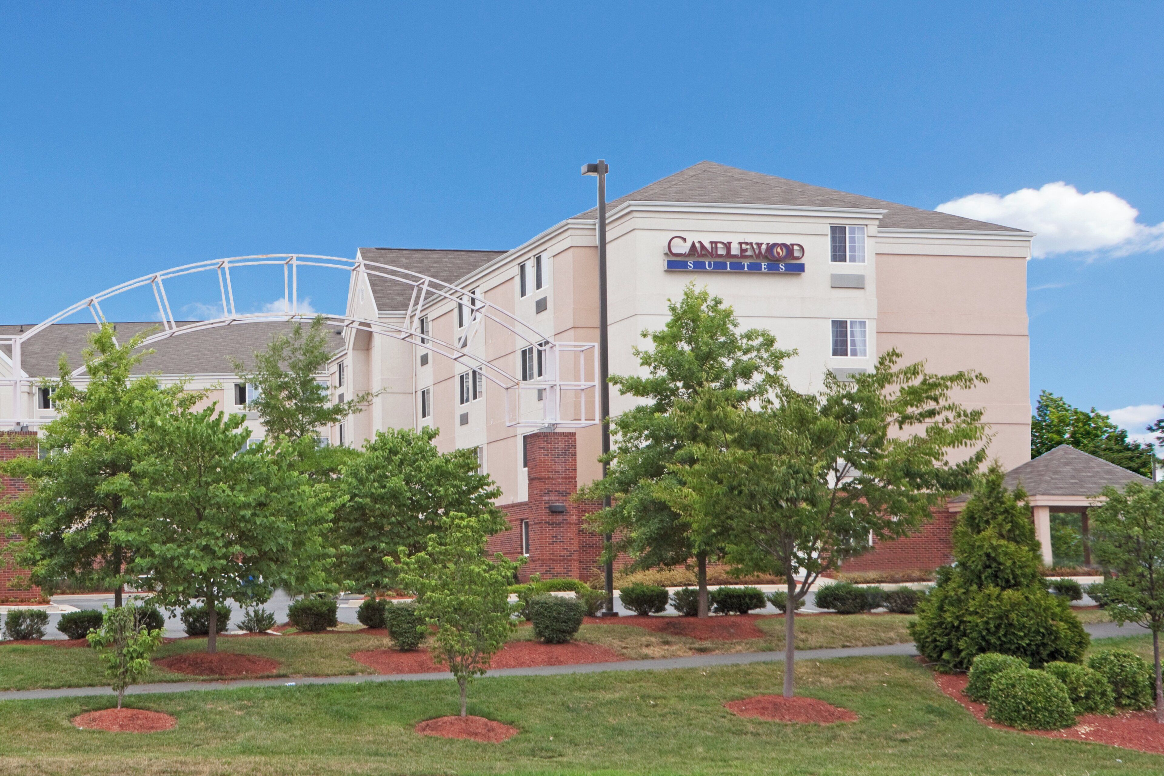 A hotel with a prominent water feature in front, a sign reading 'CANDLEWOOD SUITES', and a well-maintained lawn with trees.