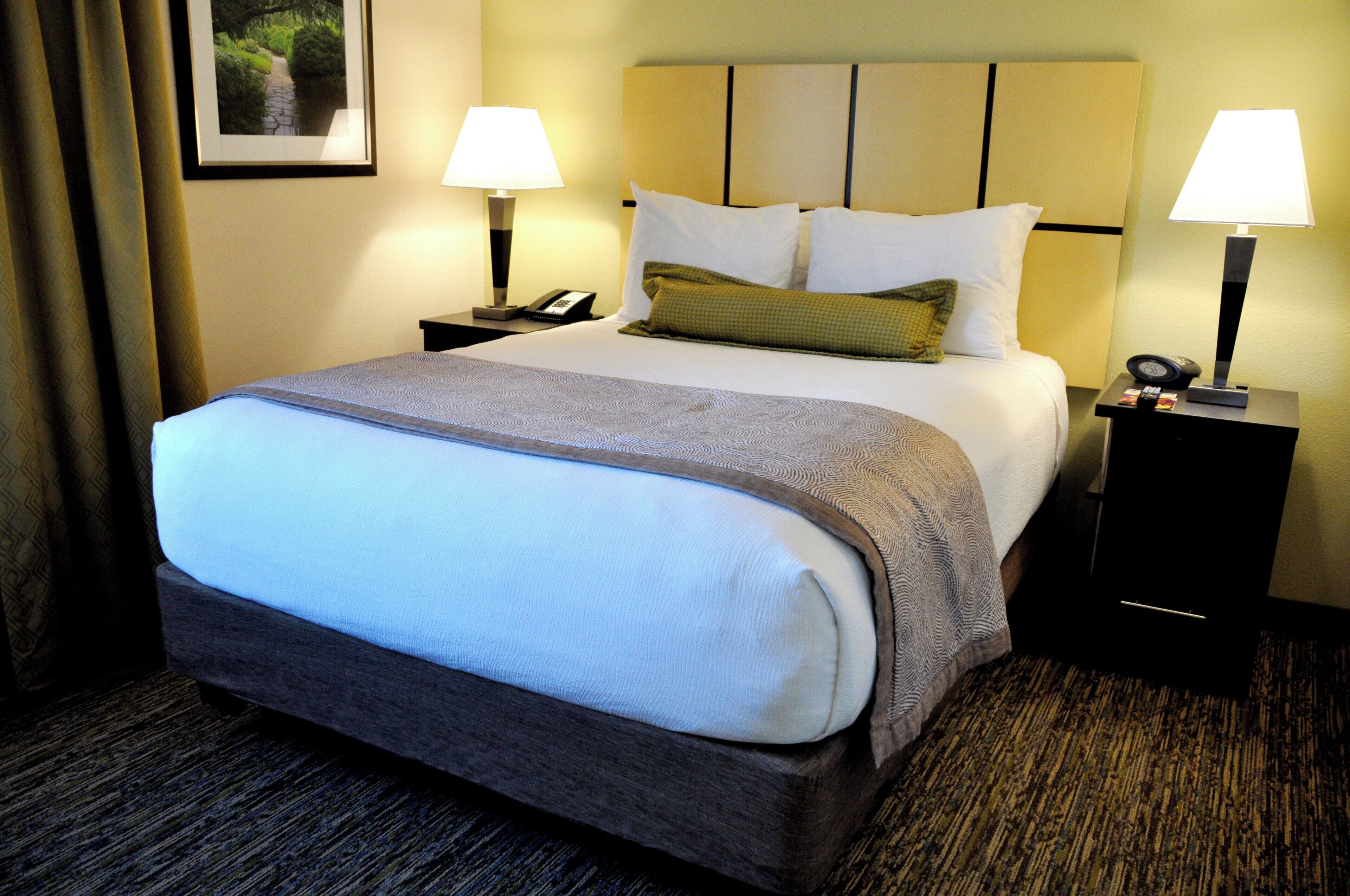 A hotel room with a large bed, two bedside tables, a nightstand, a lamp, a phone, and a clock.