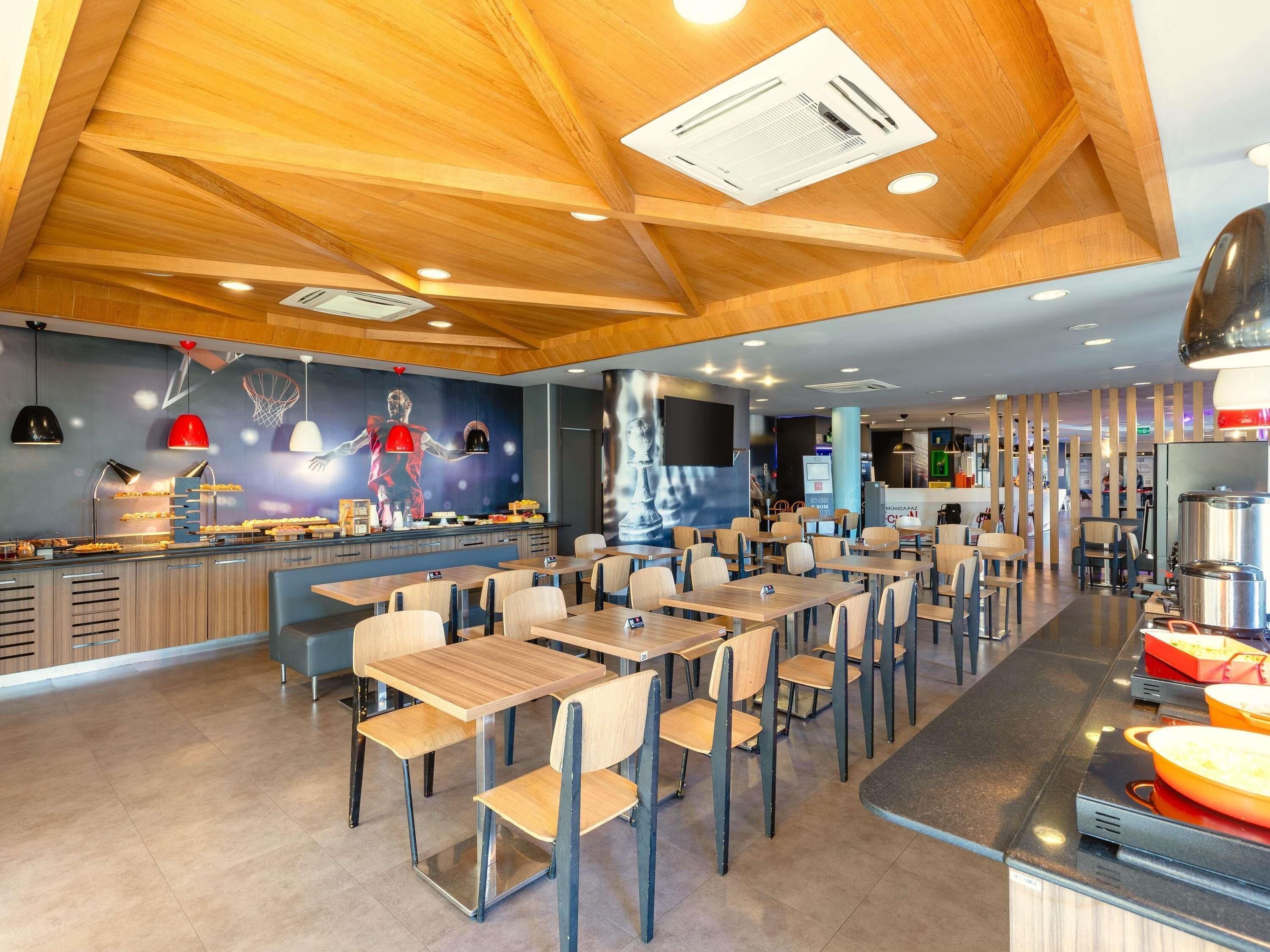 A modern restaurant with wooden ceiling beams, a counter with food display, and multiple seating areas.