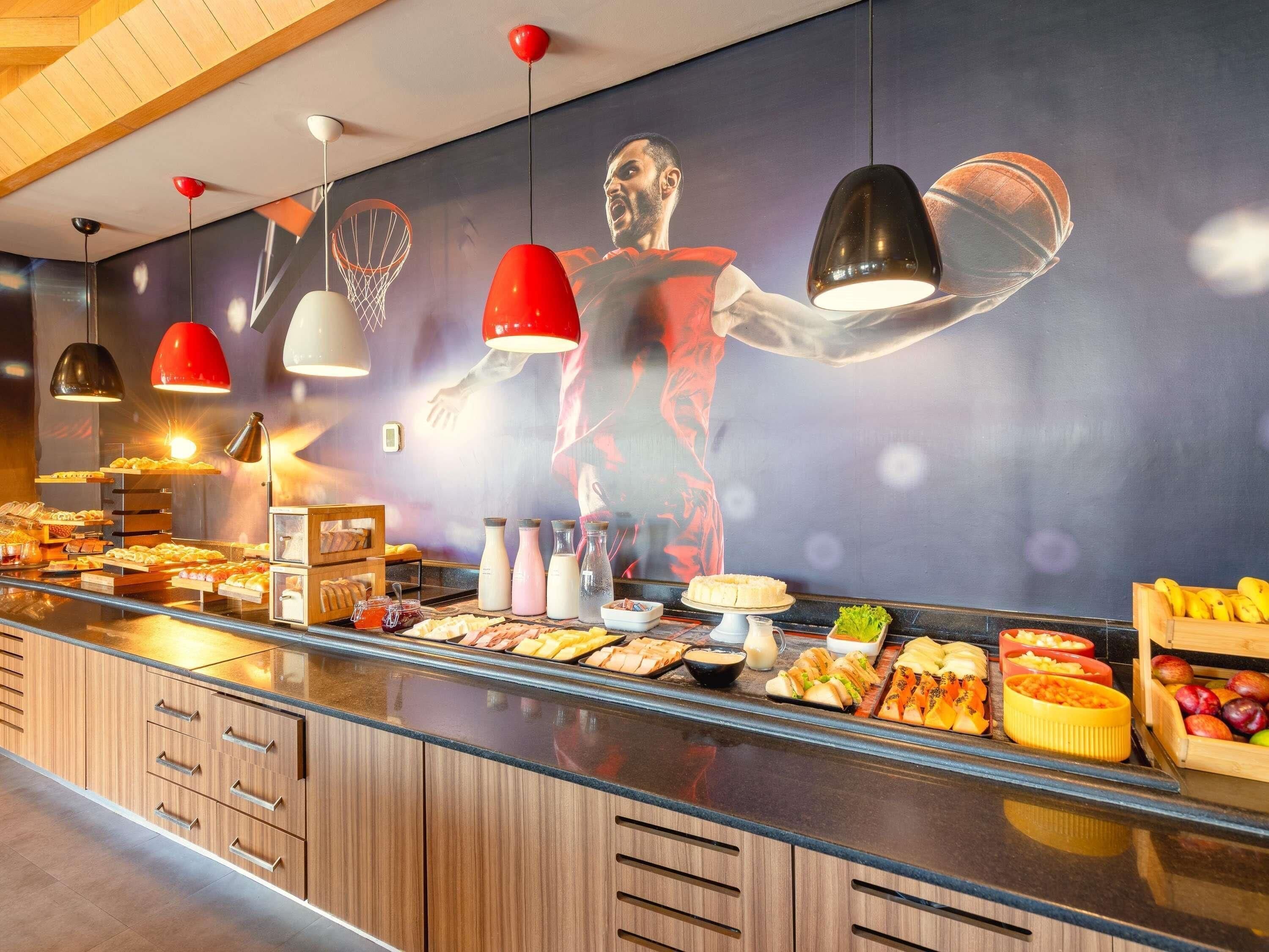 Espaço de buffet com diversos alimentos, um grande mural e iluminação pendente.