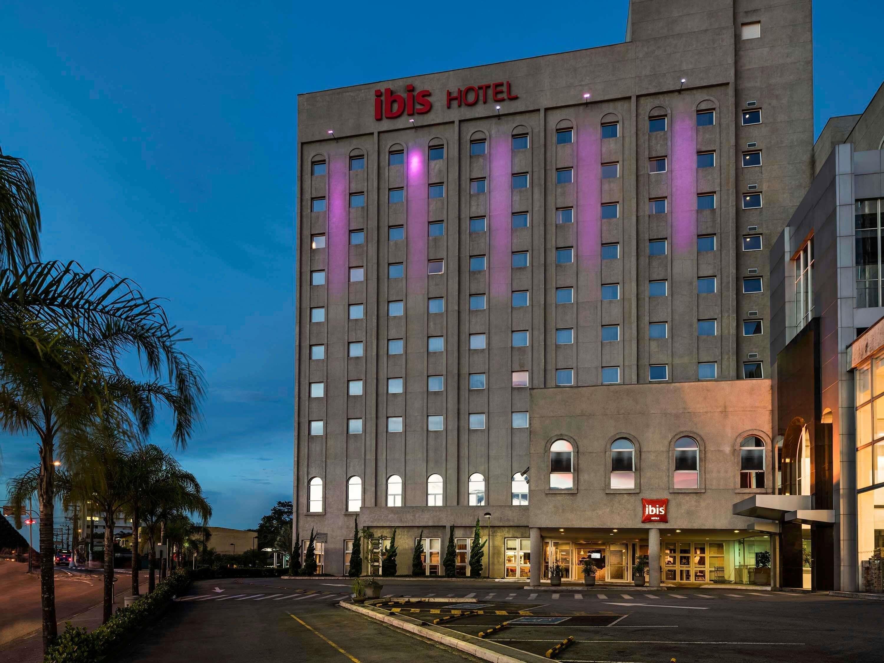 Un grand bâtiment d’hôtel, avec une enseigne « IBIS HOTEL » bien visible, de nombreuses fenêtres et une entrée bien éclairée.