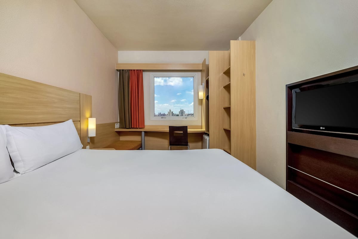 Una habitación de hotel con una cama grande, un escritorio con silla, un televisor y una ventana con cortinas.