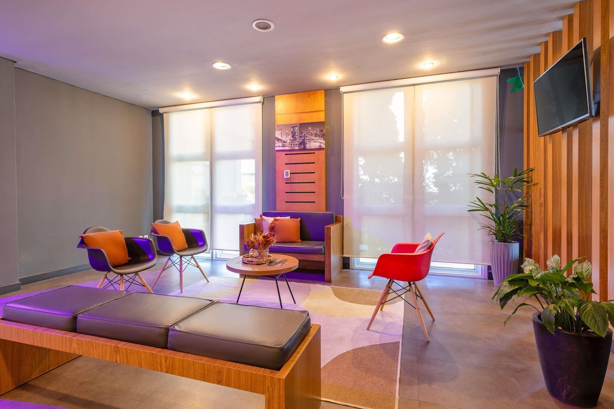 A modern lounge area with a sofa, chairs, a massage table, and potted plants.