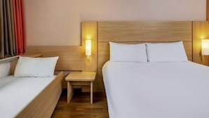 Une chambre d’hôtel avec deux lits, une petite table et deux lampes fixées au mur.