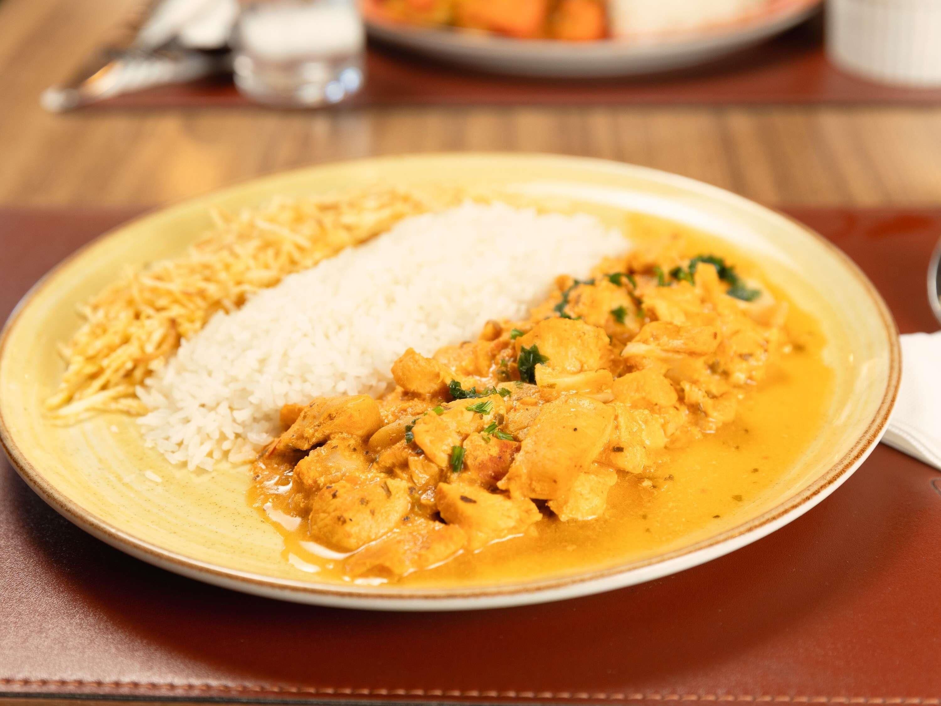 A plate of food with rice and a curry dish, possibly chicken, on a table.