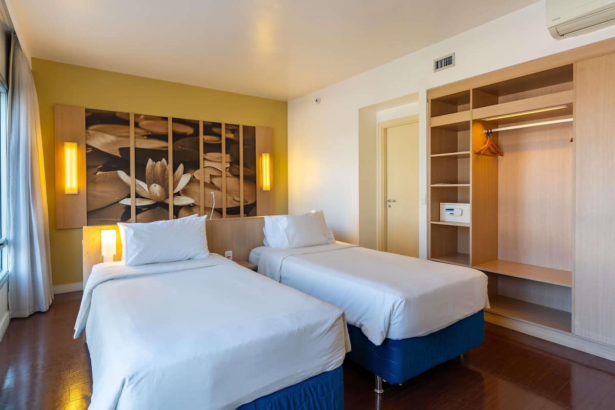 A hotel room with two beds, a wooden wardrobe, and a wall-mounted artwork.