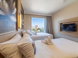 Habitación de hotel con dos camas, televisión, ventana con vista a la ciudad y un cuadro en la pared.