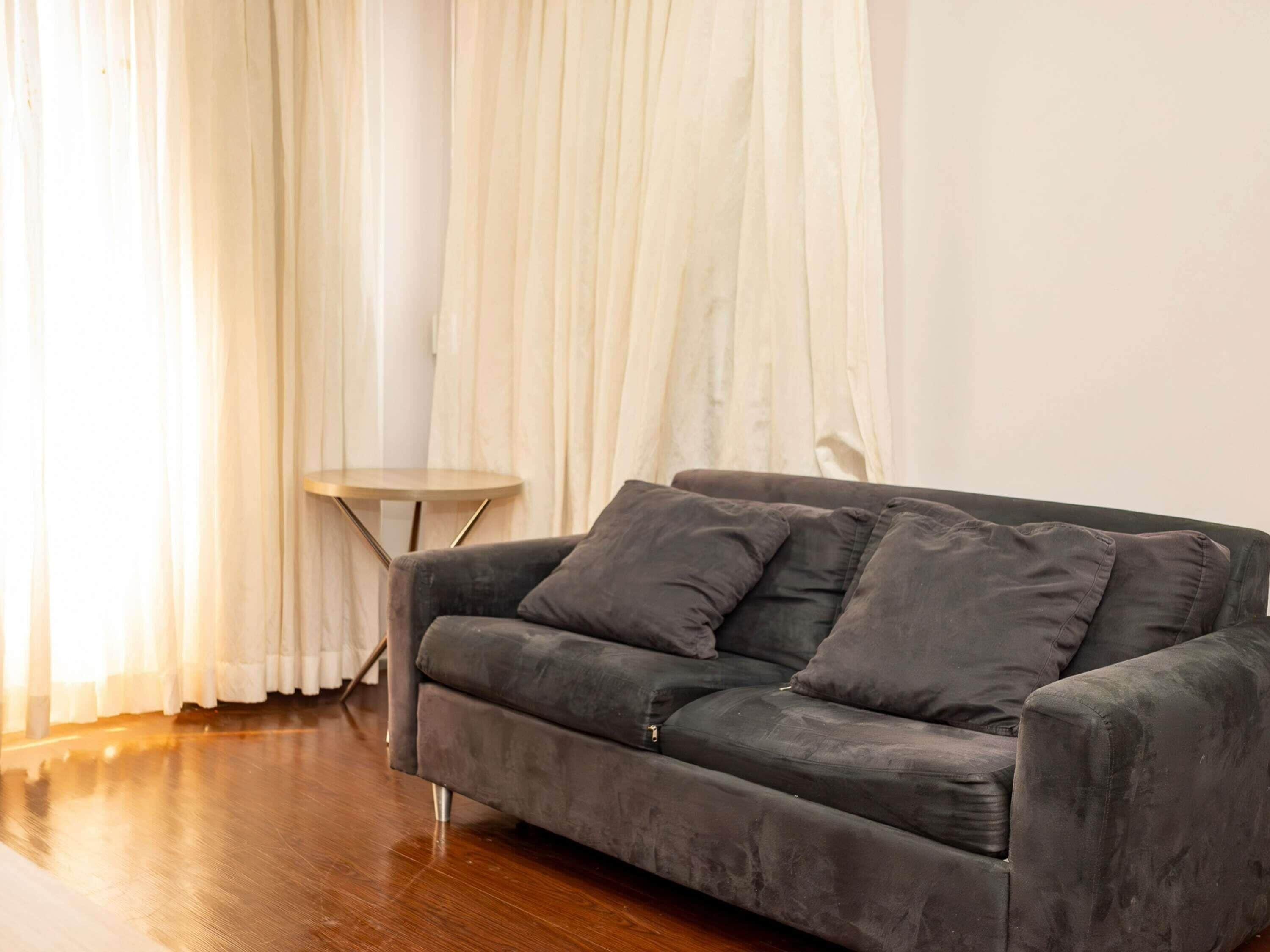 Una sala de estar moderna con un sofá gris oscuro, una mesita redonda y cortinas translúcidas.
