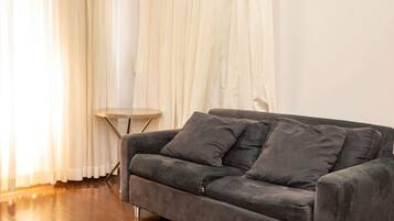 Una sala de estar moderna con un sofá gris oscuro, una mesita redonda y cortinas translúcidas.