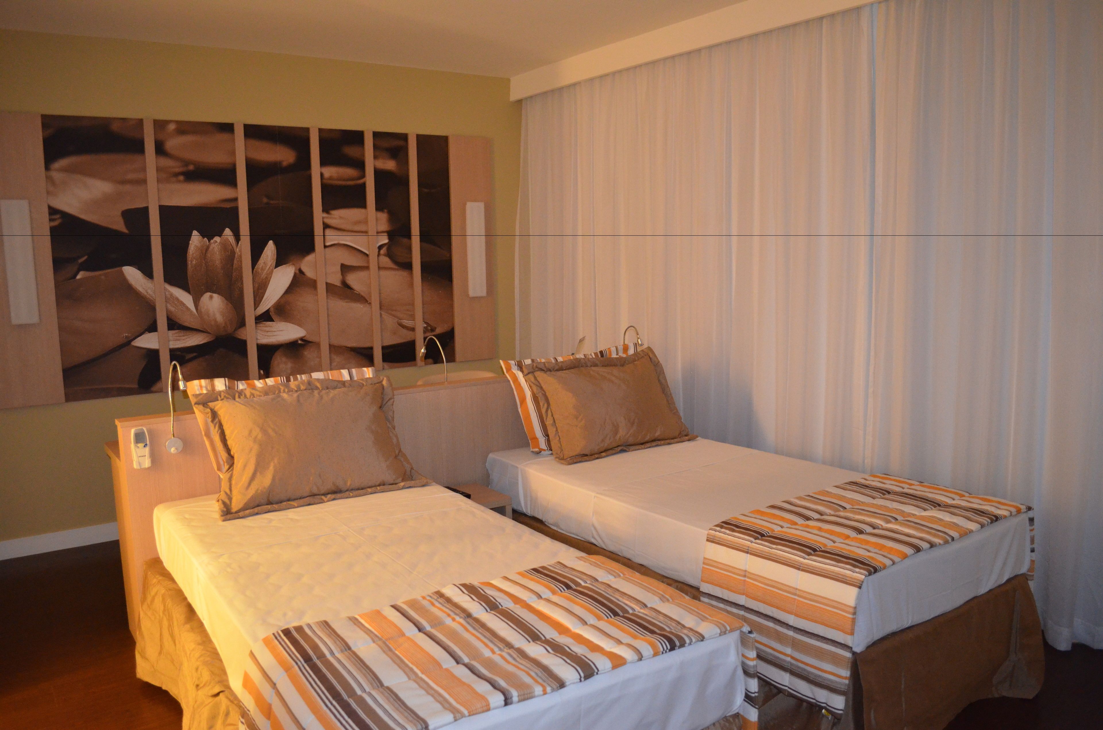 A hotel room with two beds, a large floral artwork on the wall, and a window with curtains.