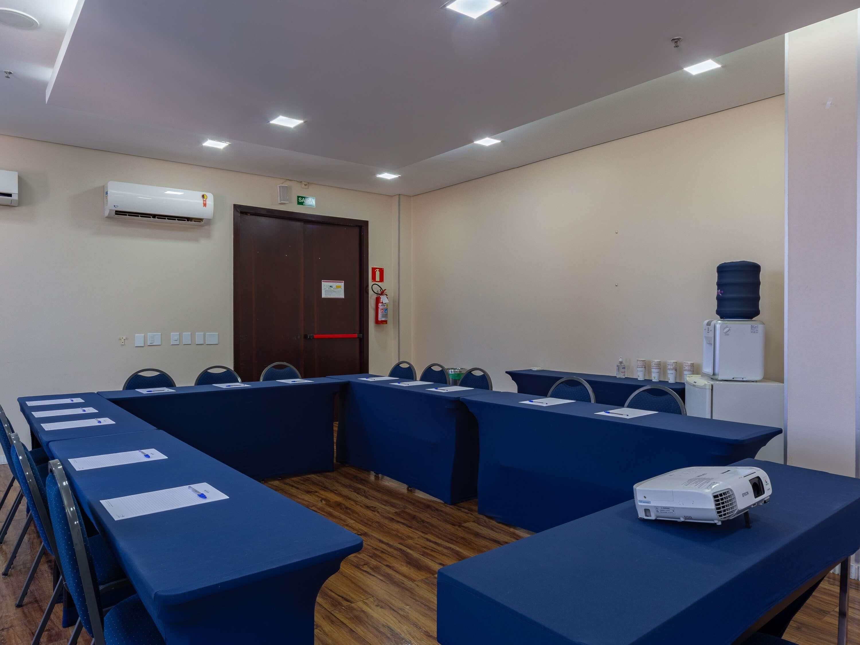 Un salón de conferencias con mesas, sillas, un proyector y un dispensador de agua.