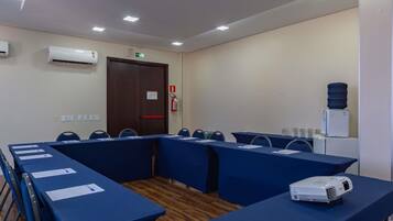 Un salón de conferencias con mesas, sillas, un proyector y un dispensador de agua.